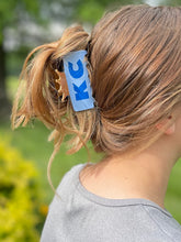 Load image into Gallery viewer, Blue KC claw clip with Royals crown detail holding woman's hair