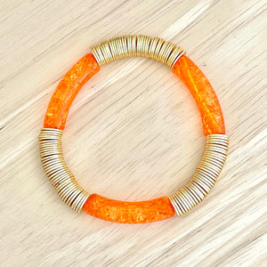 Orange bracelet with gold and silver accents on a light wood surface