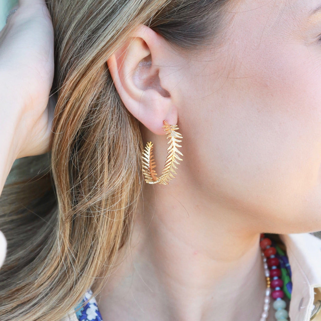 Close-up of a person wearing gold leaf earrings with a colorful necklace.