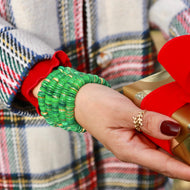 Person holding a gold gift box with a red bow, wearing a green beaded bracelet.