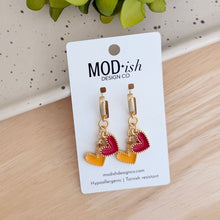 Load image into Gallery viewer, The only pair of earrings you'll reach for on Chiefs game days!  18k gold plated huggie hoops with a red enamel heart and a yellow enamel heart charm.  
